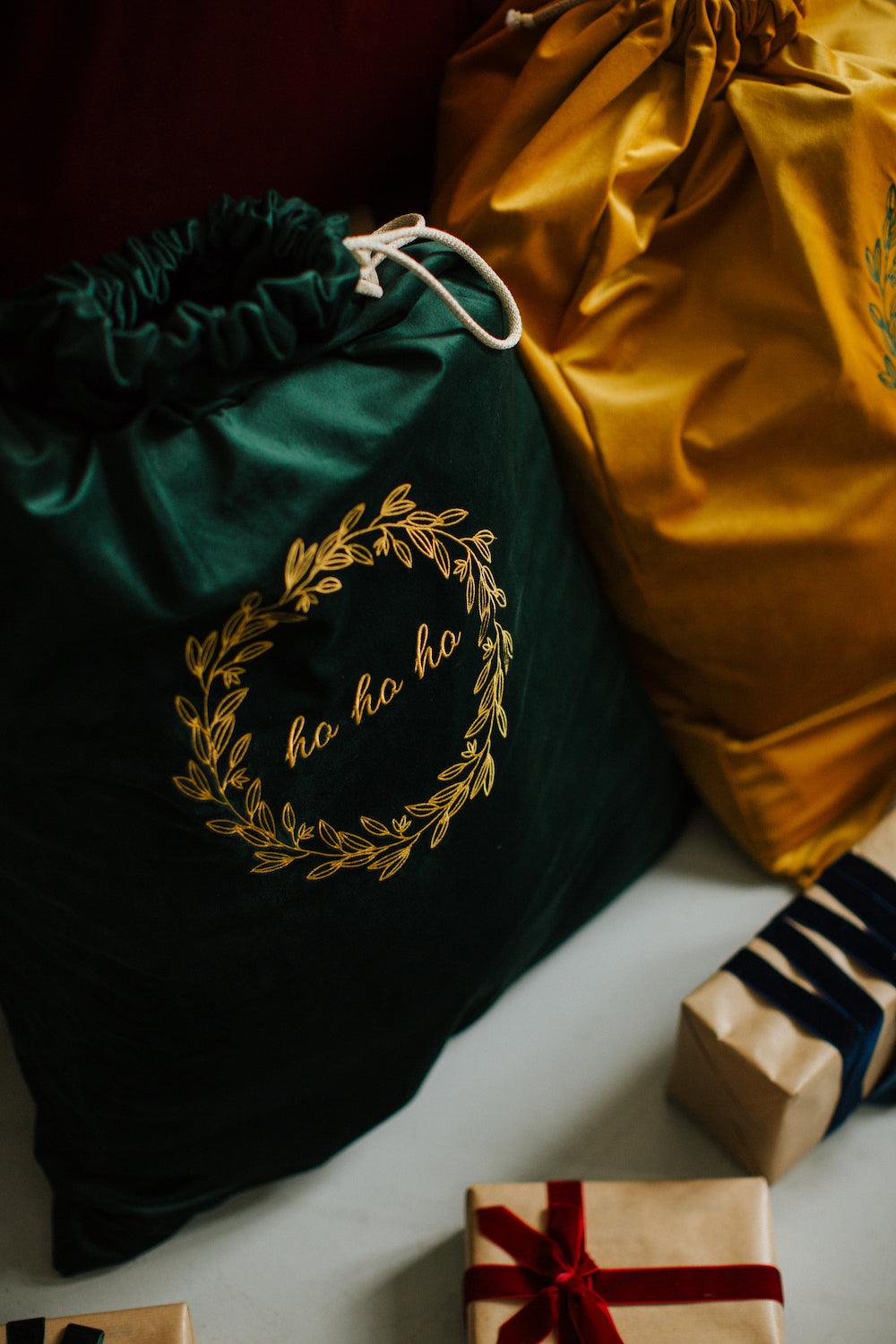 Green velvet christmas sack with embroidered ho ho ho by Bettys Home next to yellow christmas sack 