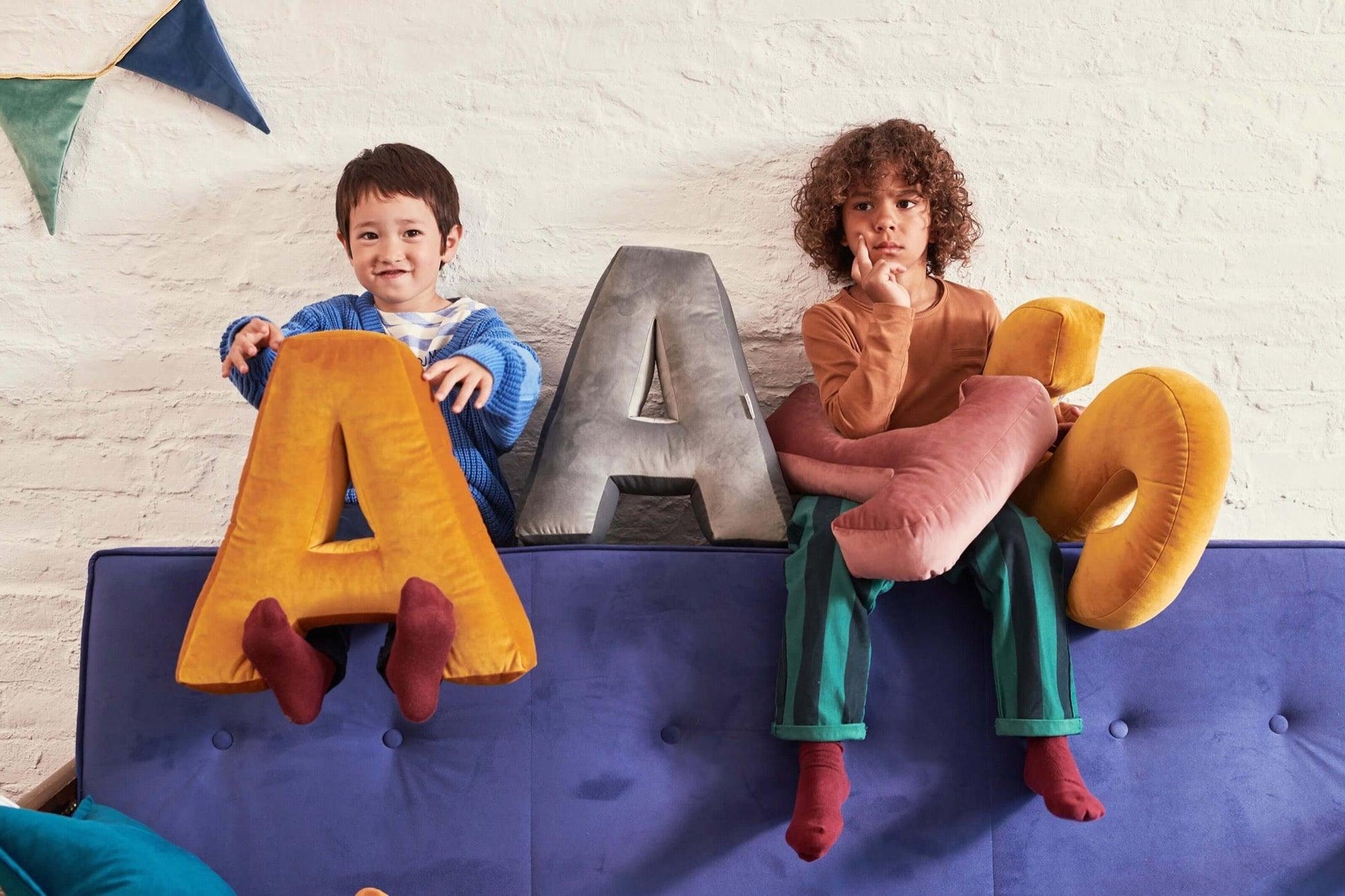 two kids sitting on sofa with velvet letter cushion in yellow colour by betty's home
